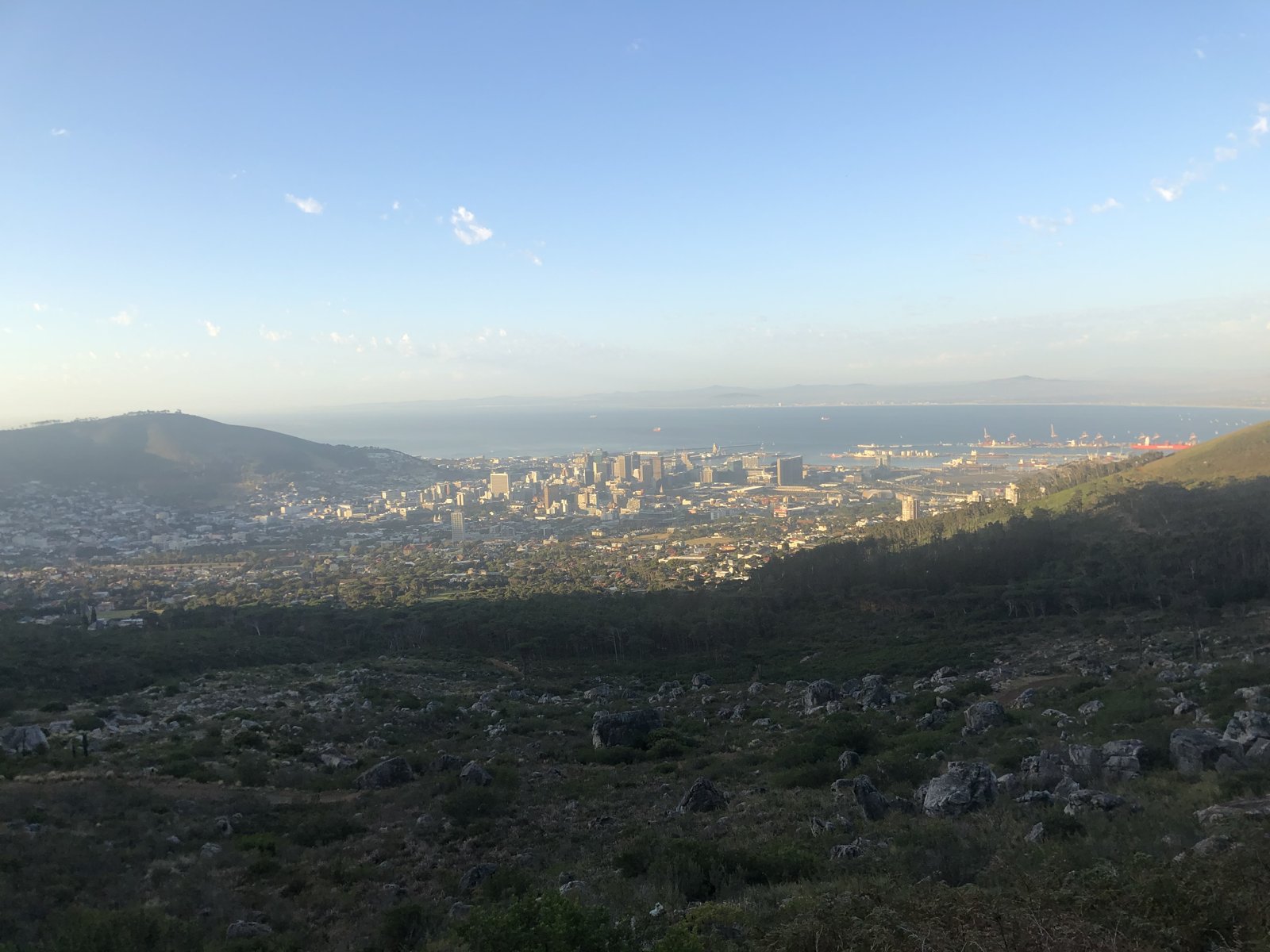 Cape Town seen from the mountainside — city, ocean, and wild rocky foreground
